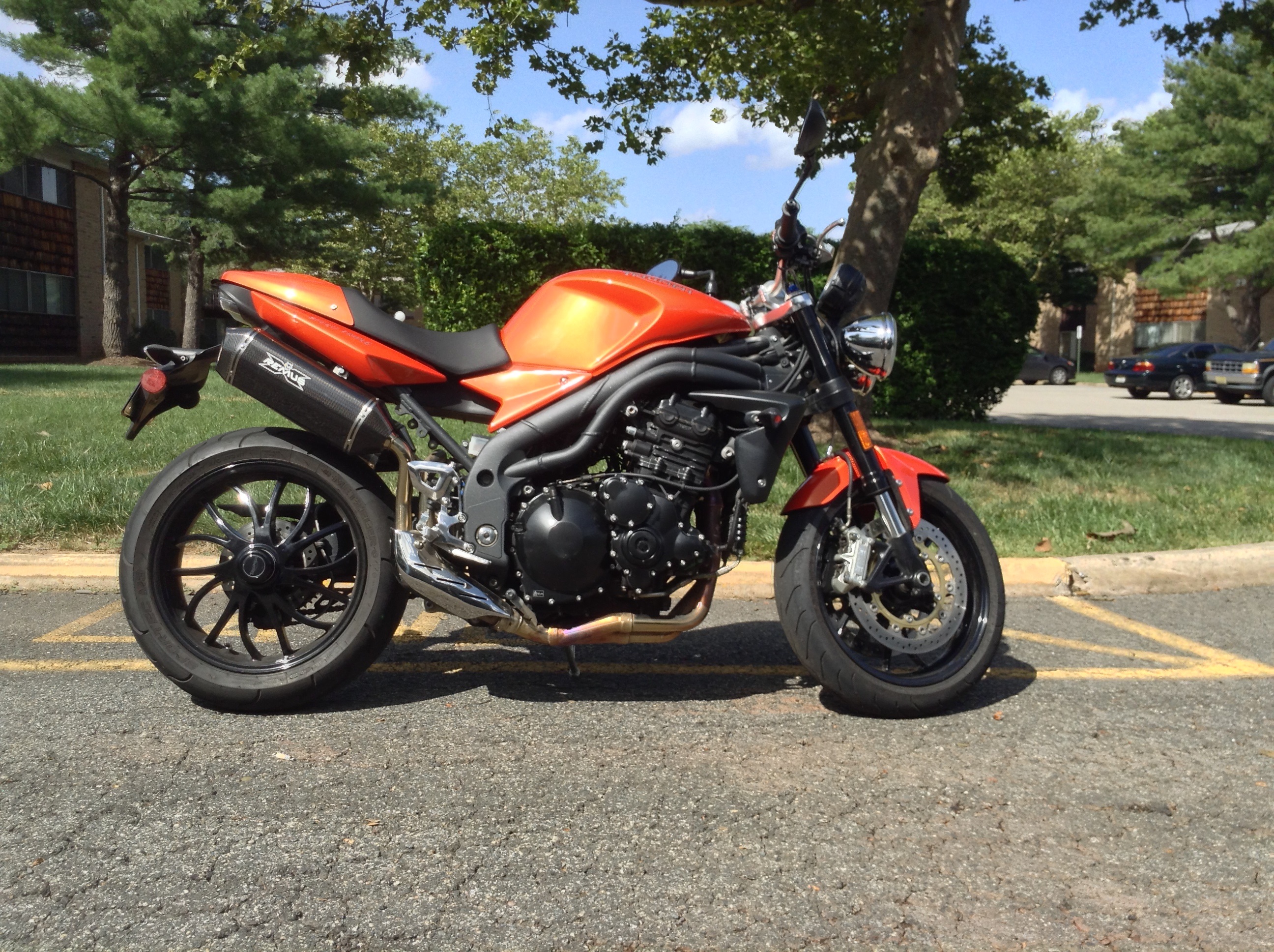 An orange 2010 Triumph Speed Triple 1050 in a parking lot on a nice day